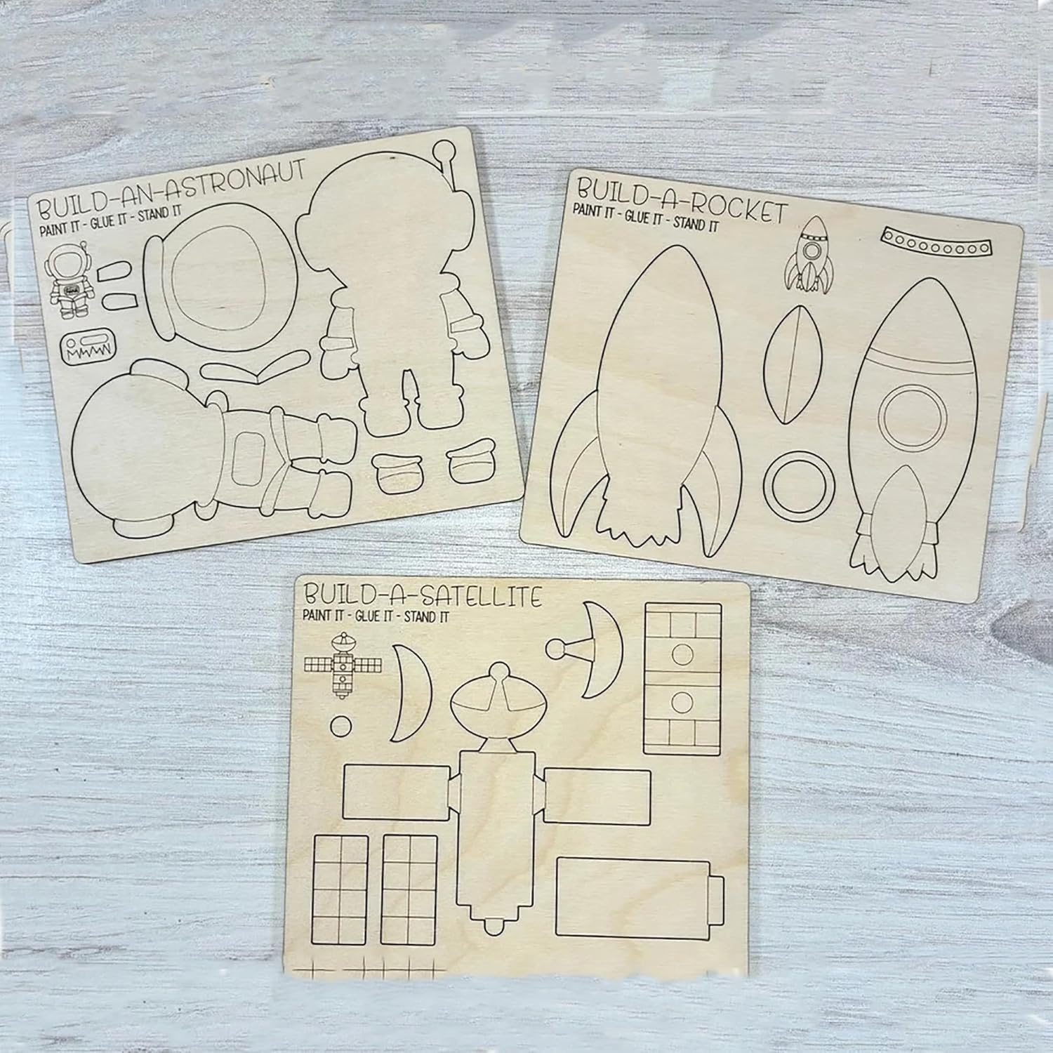 Wooden cutouts of astronaut, rocket, and satellite with assembly lines on a light wooden surface.