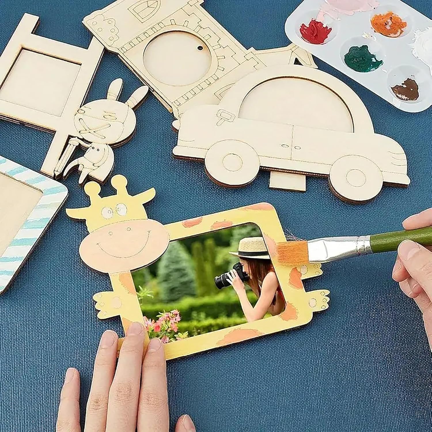 Wooden picture frames with animal designs on a blue surface, with a hand painting one of them.