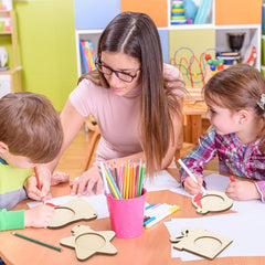 Teacher assisting two children with coloring activities in a classroom setting.