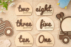 Wooden milestone markers for baby's first year with text indicating months.