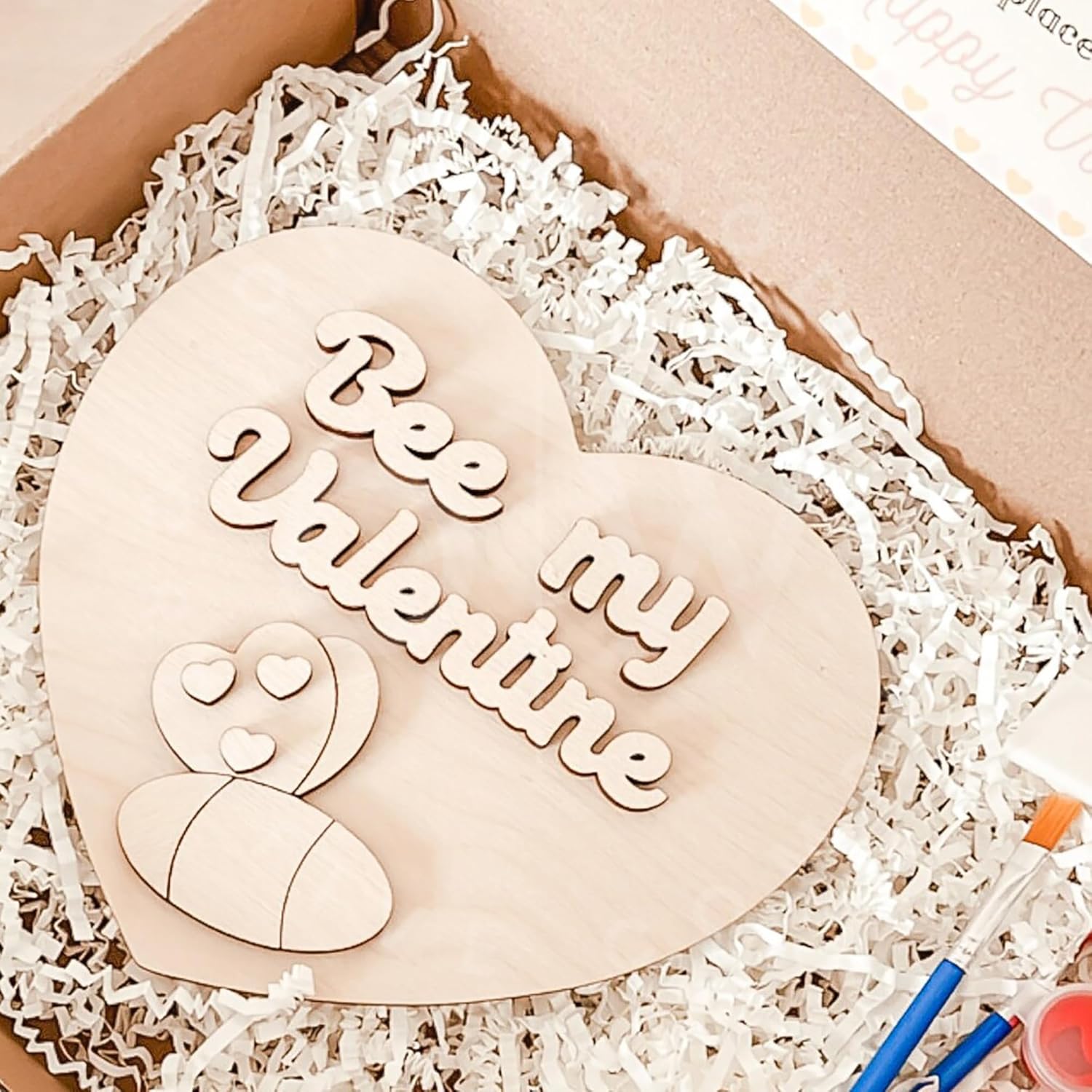 Heart-shaped wooden plaque with 'Bee my Valentine' text on a white crinkled paper background