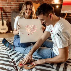 Man and woman sitting on a bed, looking at a laptop together.