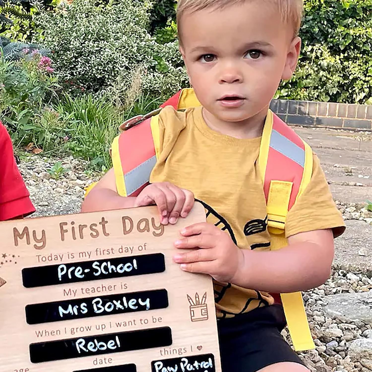 Child holding a sign for their first day of pre-school outdoors.