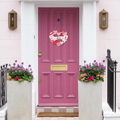 Pink door with decorative heart sign and flower pots on a white wall.