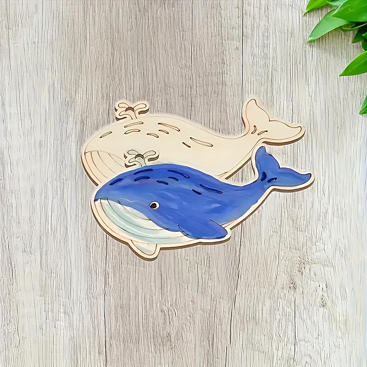 Blue whale cutout on a wooden surface with green leaves in the corner
