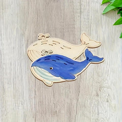 Blue whale cutout on a wooden surface with green leaves in the corner
