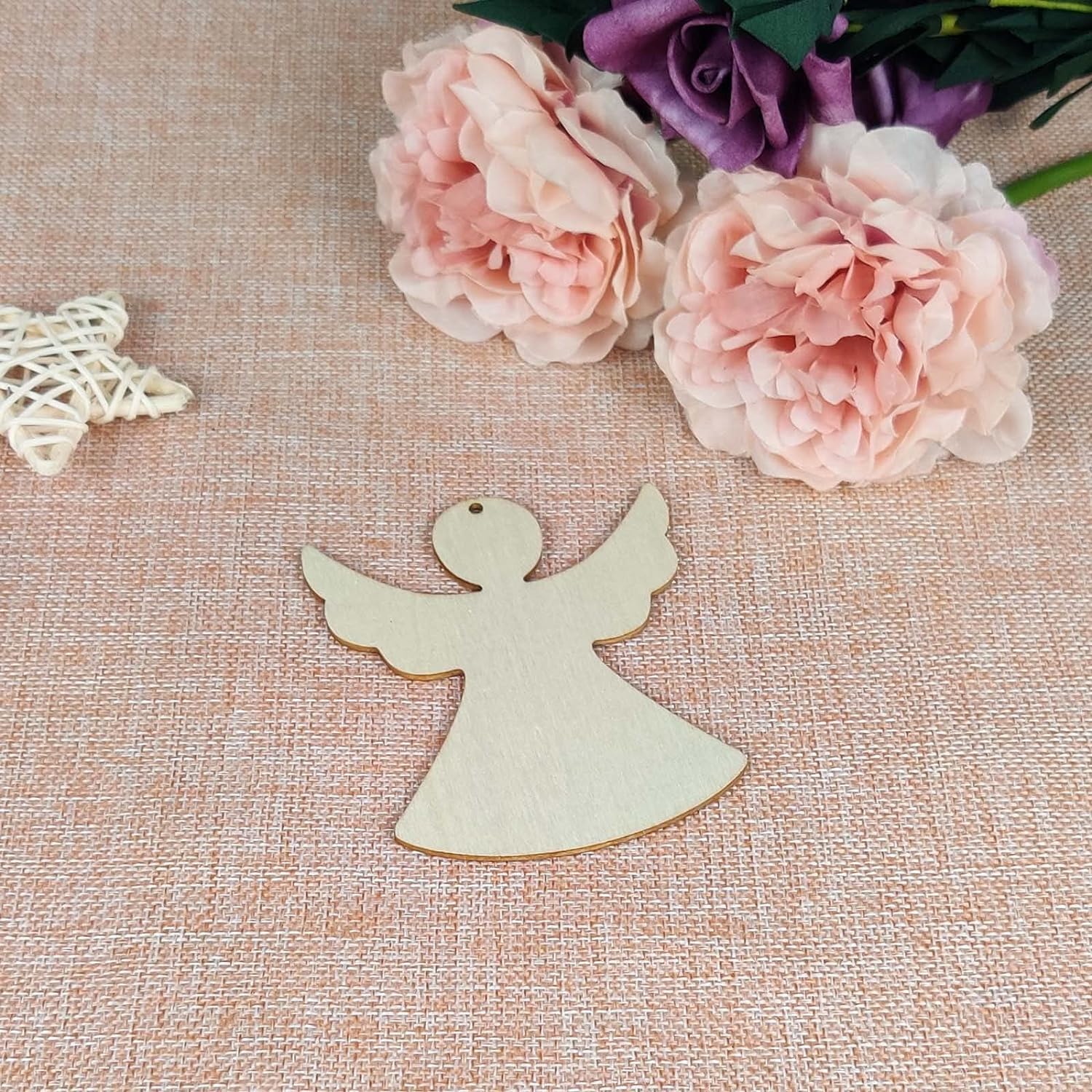 Wooden angel ornament on a textured surface with pink flowers and a decorative star.