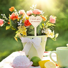 Floral arrangement with a heart-shaped sign and a mug on a table outdoors.
