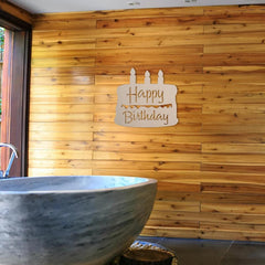Wooden 'Happy Birthday' sign on a wooden wall with a stone bathtub in the foreground.