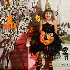 Child in Halloween costume holding a pumpkin with decorative pumpkins and ghosts in the background.