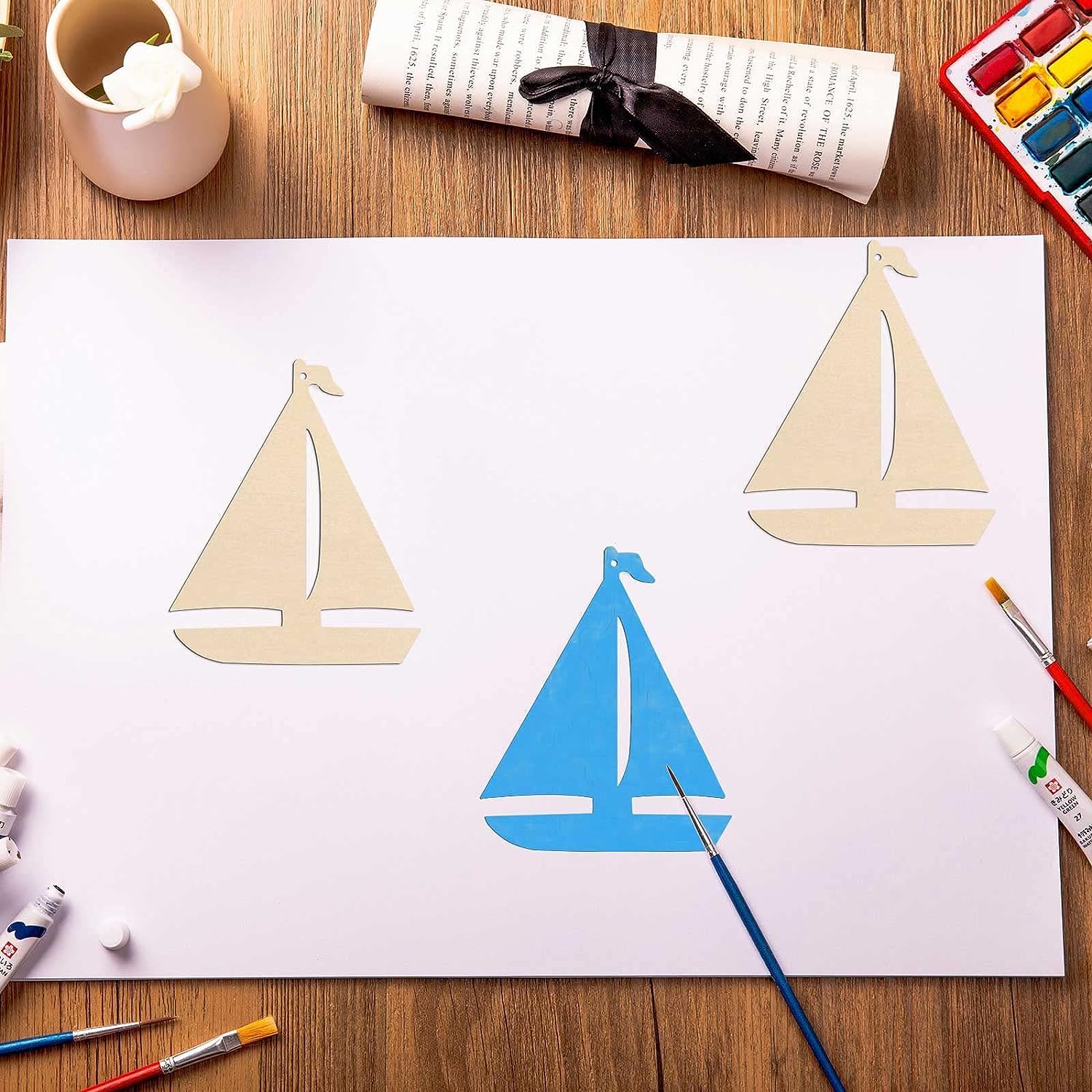 Children's drawing of sailboats on a piece of paper with art supplies around.