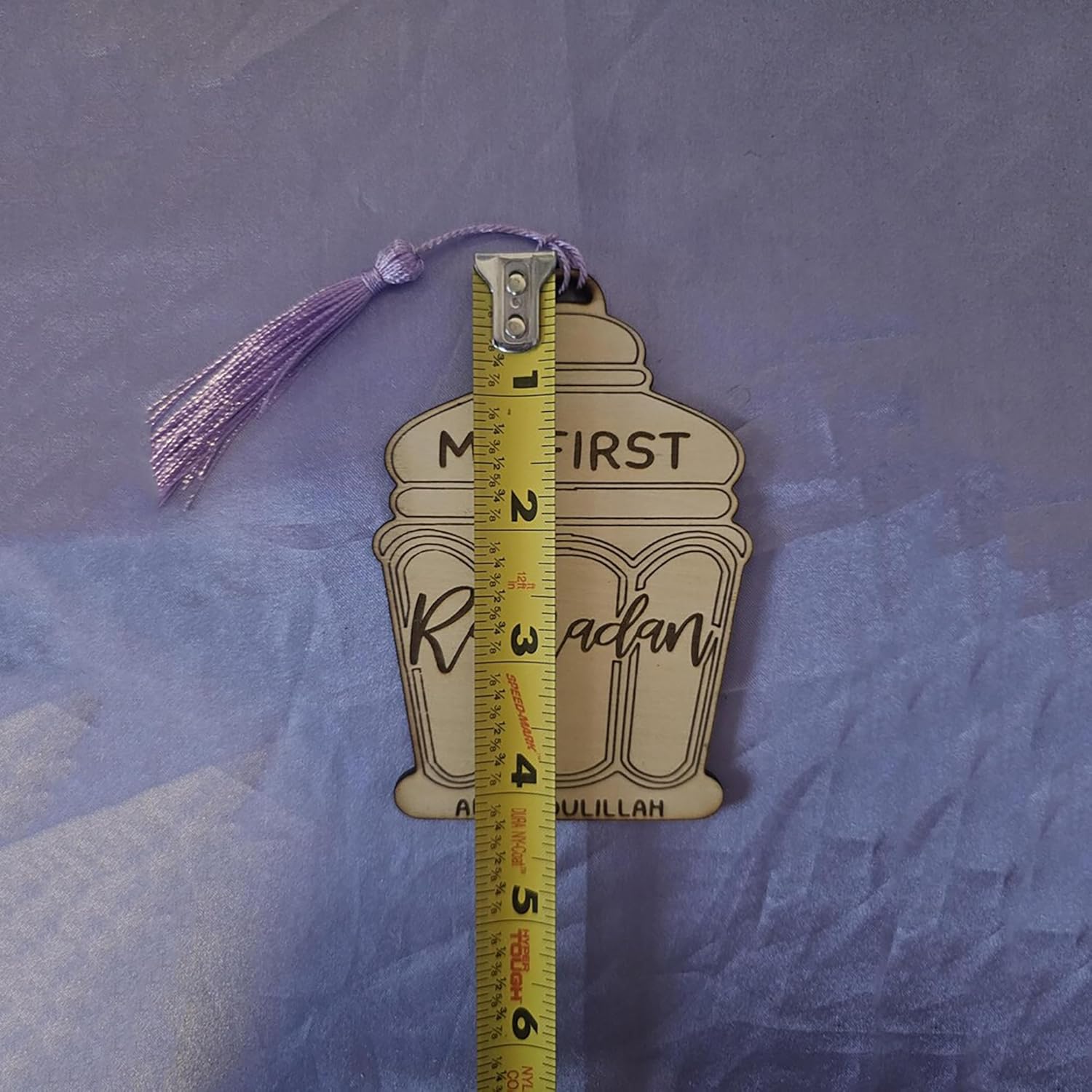 Decorative tag with tassel and measurement ruler on a textured purple background