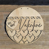 Wooden round decorative item with 'Be My Valentine' text and heart designs on a wooden surface.