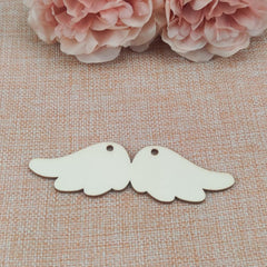 Two wooden angel wing shapes on a textured fabric background with pink flowers.
