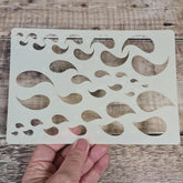 Stencil with wavy line pattern held by a hand on a wooden surface