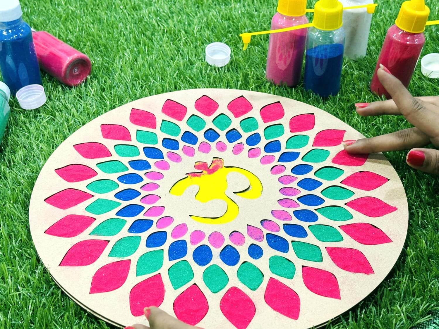 Colorful mandala on a wooden board with paint bottles and brushes on grass