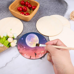 Person painting a colorful design on a round ceramic product with a brush, surrounded by ingredients on a marble surface.