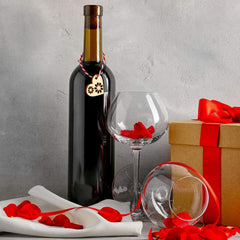 Bottle of red wine with a decorative heart tag, two glasses, and a gift box on a gray surface.