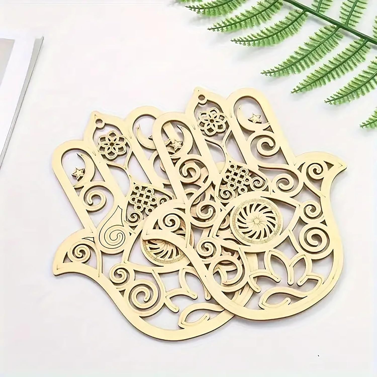 Decorative wooden Hamsa hand with intricate patterns on a white surface with green leaves.