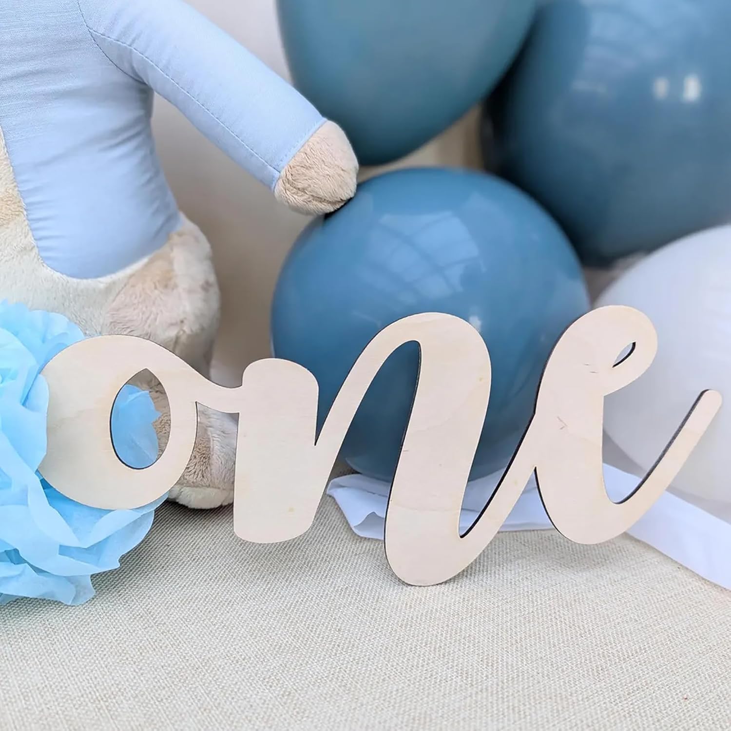 Wooden 'one' sign with blue balloons and a plush toy in the background