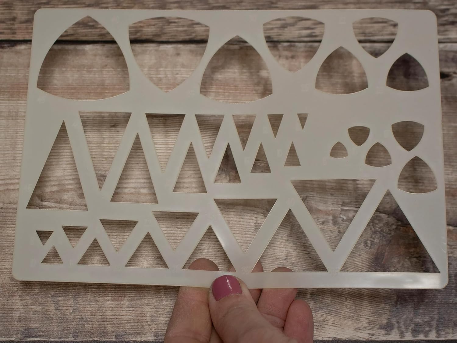 Geometric patterned stencil held by a hand on a wooden surface