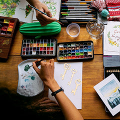 Artistic workspace with watercolor paints, brushes, and art supplies on a wooden table.