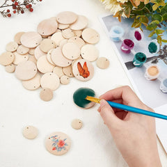 Wooden discs with painted designs on a white surface, with a hand using a paintbrush.