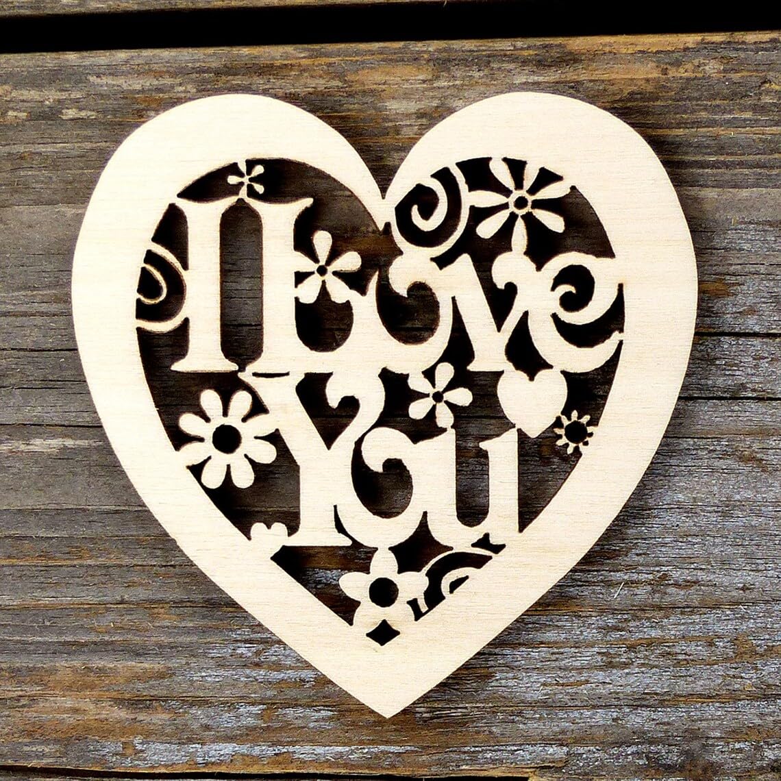 Wooden heart-shaped cutout with 'I ❤️ love you' engraving on a wooden background