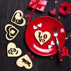 Red plate with heart-shaped 'LOVE' cutout, red gift box, and decorative flowers on a dark wooden surface.