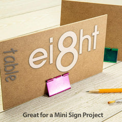 Cardboard sign with 'eight' and 'table' text on a wooden surface with stationery items.