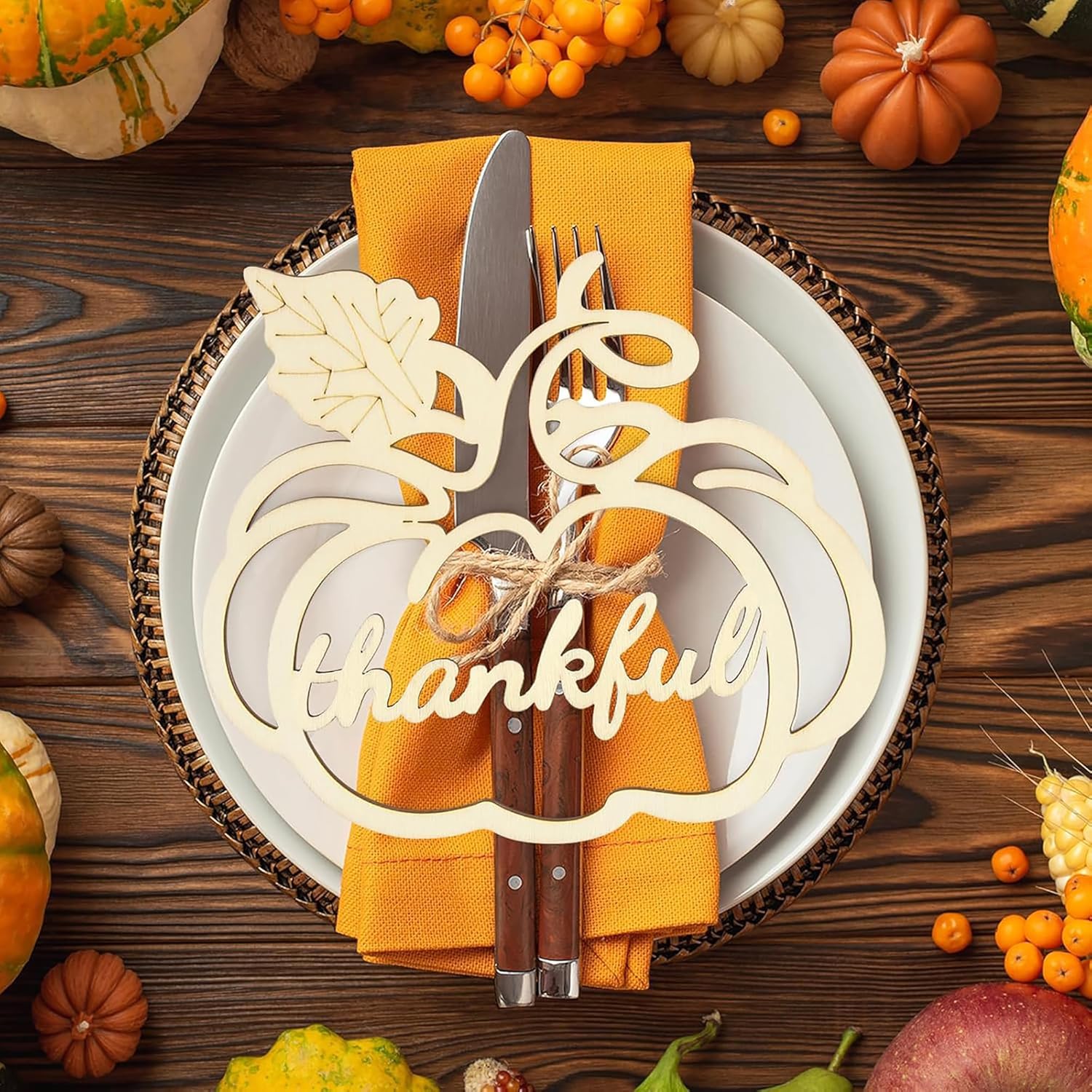 Thanksgiving table setting with 'thankful' placemat, knife, and fork on a wooden table with pumpkins and corn.