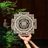 Decorative Sri Yantra symbol held between hands with greenery in the background