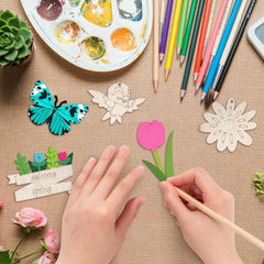Hands working with paper cutouts of a butterfly, flower, and fairy on a textured surface with art supplies.