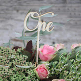 Wooden 'One' cake topper on a floral arrangement with pink roses and greenery.