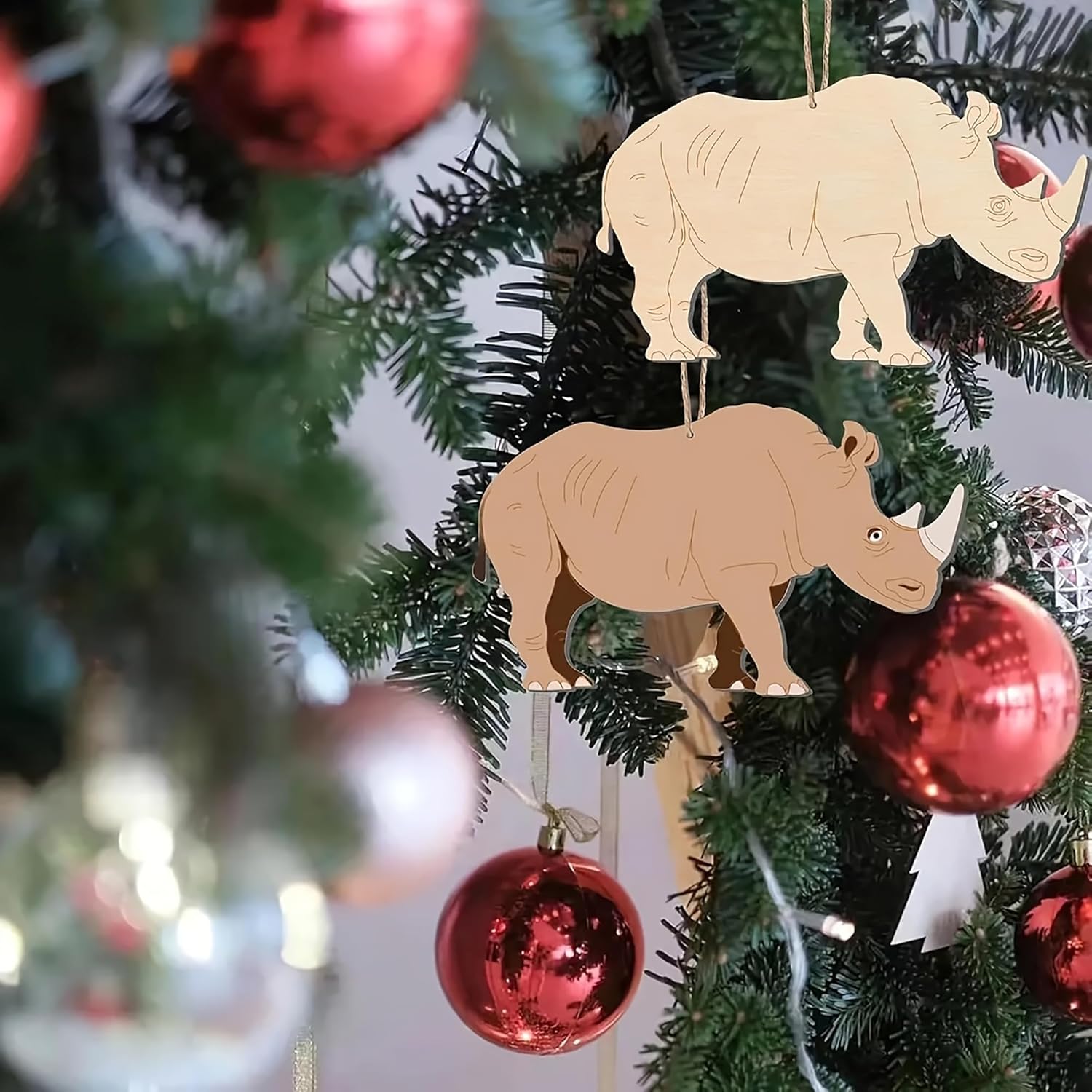 Two rhinoceros ornaments hanging on a Christmas tree with red balls.