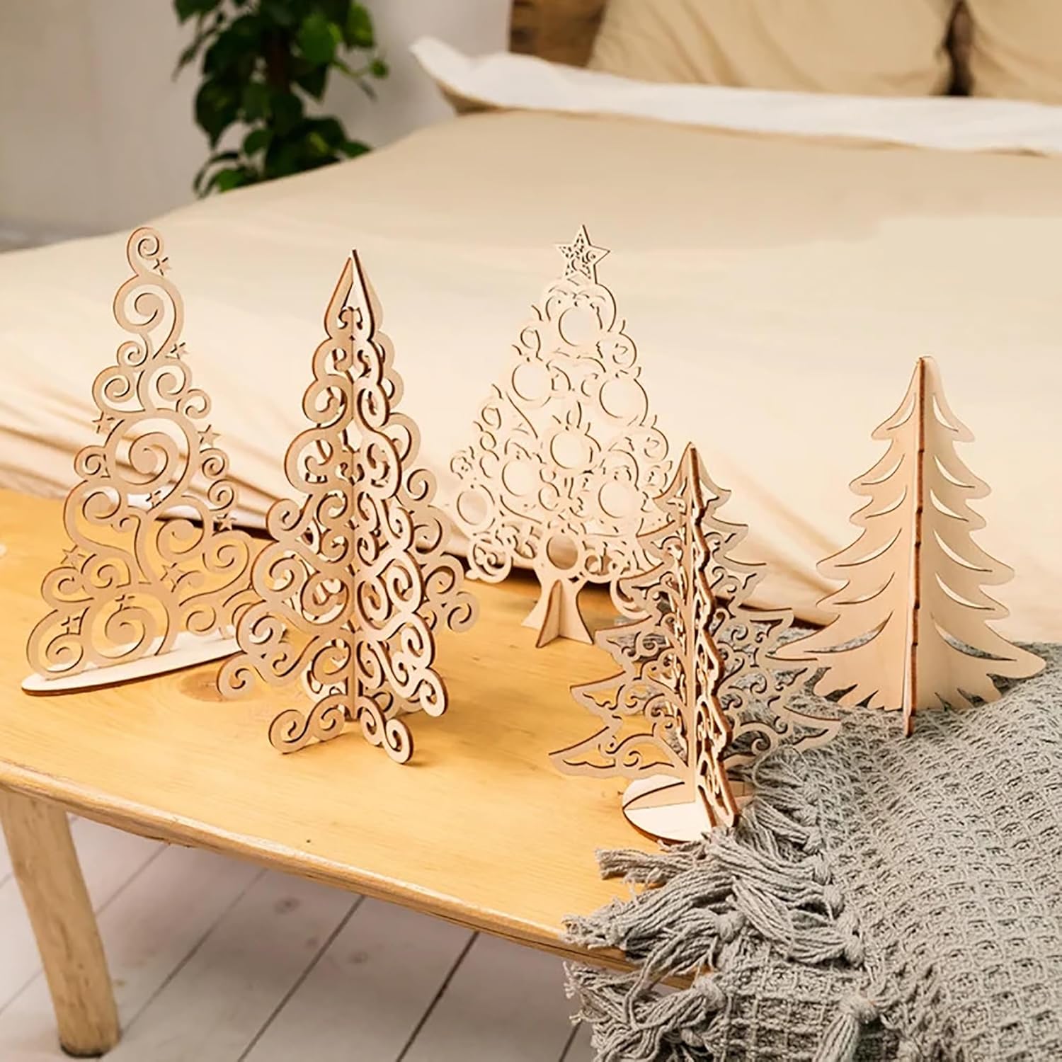 Set of decorative wooden Christmas trees on a wooden surface with a soft blanket and pillow in the background.