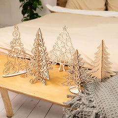 Set of decorative wooden Christmas trees on a wooden surface with a soft blanket and pillow in the background.