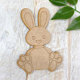 Wooden bunny cutout on a wooden surface with green leaves