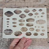Hand holding a stenciling template with geometric shapes on a wooden surface
