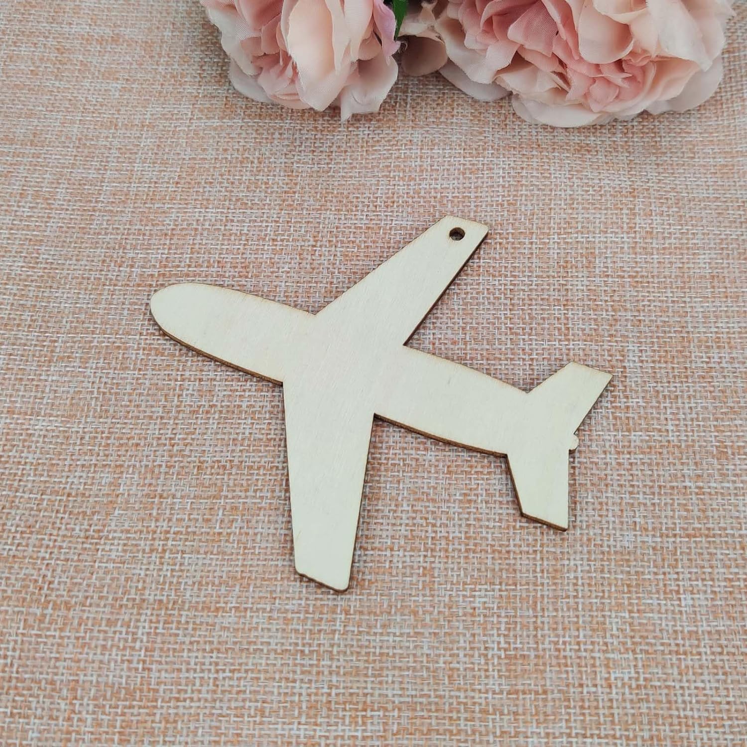Wooden airplane shape on a textured surface with pink flowers in the background