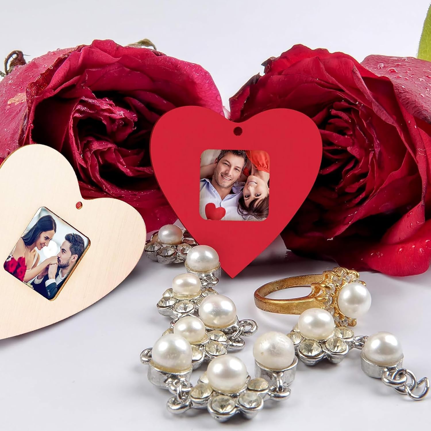 Heart-shaped photo frames with a couple's picture, red roses, and jewelry on a white background