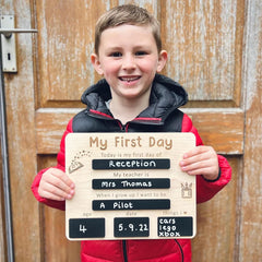 Child holding a sign for their first day of school in front of a wooden door.