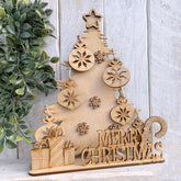 Wooden Christmas tree decoration with 'Merry Christmas' text on a light wooden background.