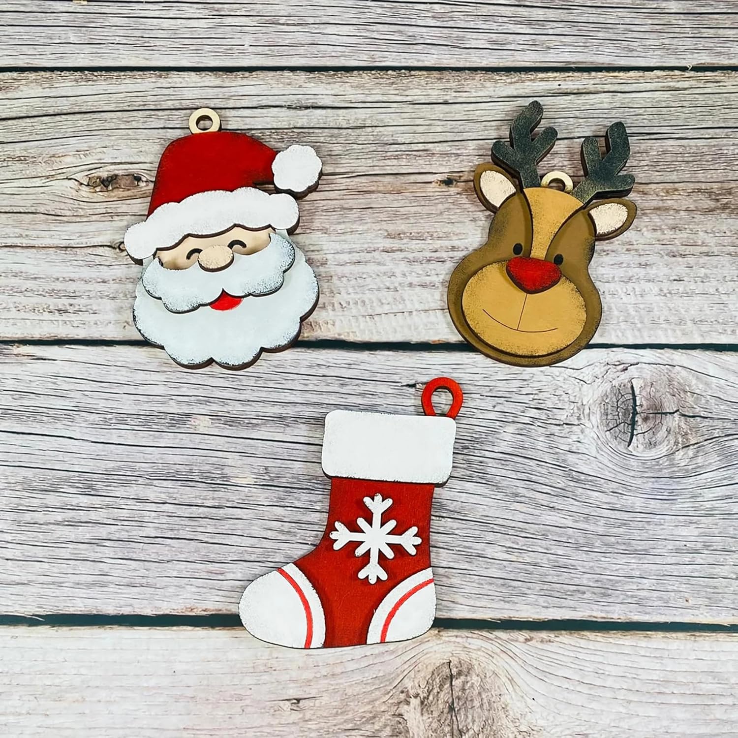 Decorative Christmas ornaments including a Santa Claus face, reindeer head, and red stocking with white snowflake design on a wooden background.