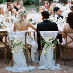 Wedding couple sitting at a decorated table with 'Mr' and 'Mrs' signs on chairs.