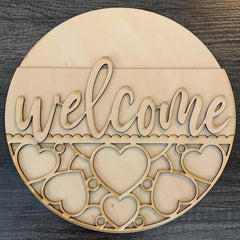 Round wooden decorative piece with 'welcome' text and heart shapes on a dark surface