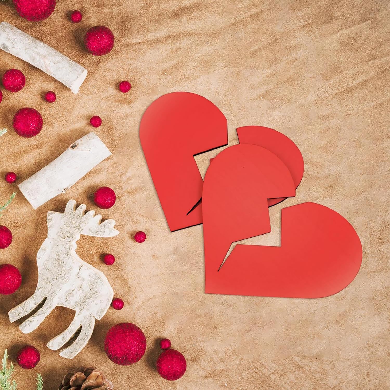 Red heart-shaped cutouts on a textured brown surface with red spherical objects and a white deer figure.