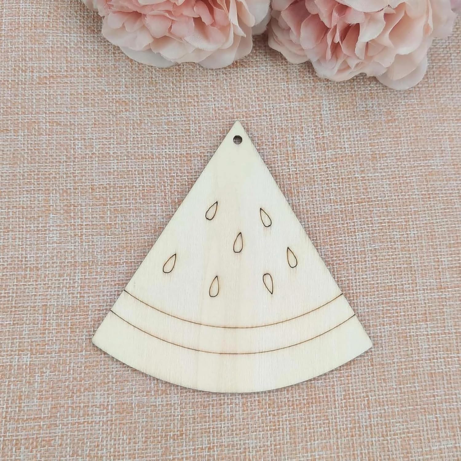 Wooden watermelon slice ornament on a textured surface with pink flowers in the background