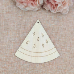 Wooden watermelon slice ornament on a textured surface with pink flowers in the background