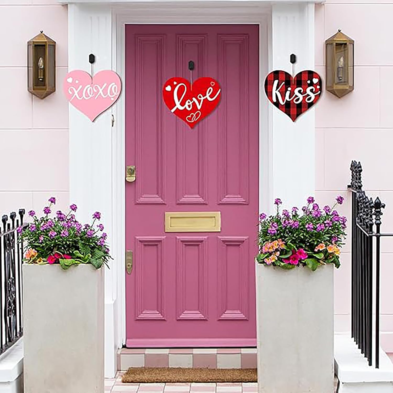Pink door with decorative hearts and flower pots on a white wall.